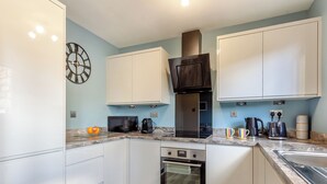 A modern kitchen with white cabinets, a black microwave, a coffee maker, and a toaster. - 2 bedroom accommodation in Nairn (Nairn)