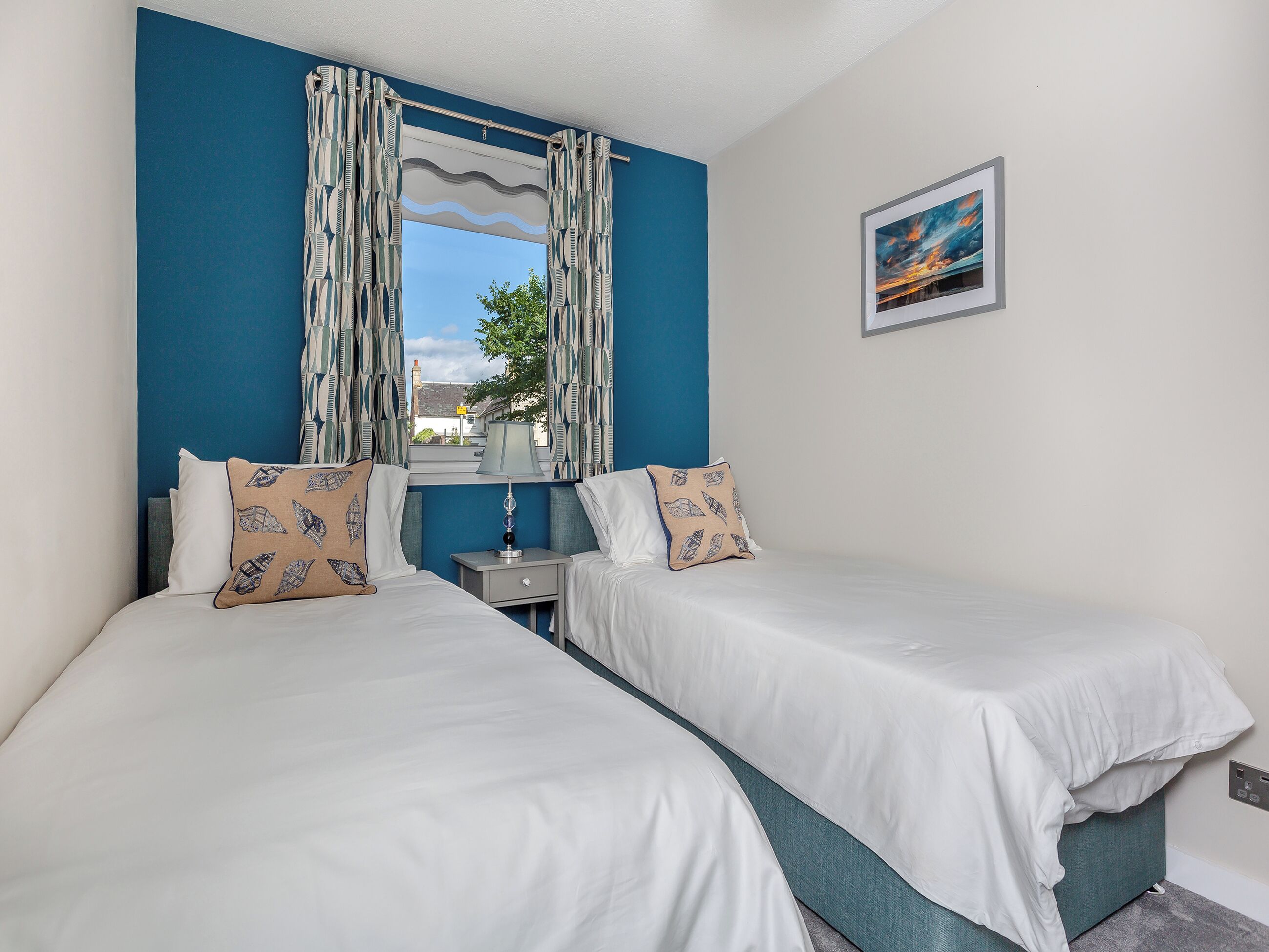 A room with two beds, a nightstand, a lamp, and a painting on the wall.