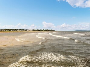 A beach with waves, a clear sky, and a distant shoreline with buildings.