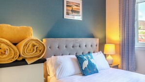 A neatly made bed with white linens, a blue pillow with a bird design, and rolled towels on a side table. - 2 bedroom accommodation in Nairn (Nairn)