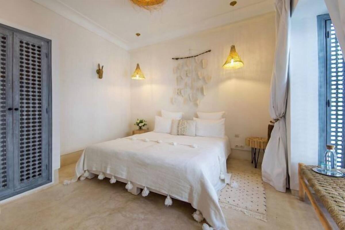 A bedroom with a bed, a wardrobe, a wall-mounted light fixture, and a window with a curtain.