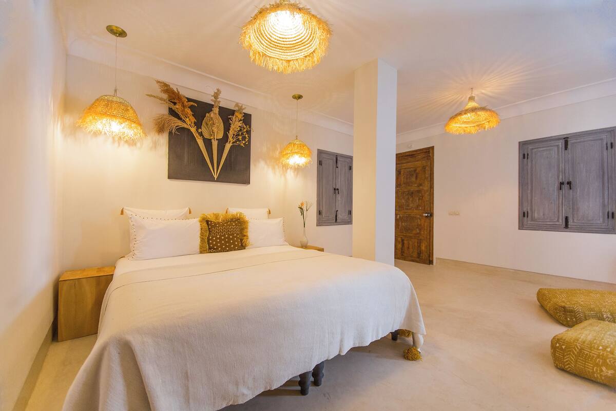A spacious bedroom with a large bed, two bedside tables, and a wooden door.