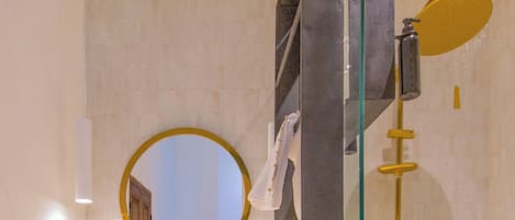 Un baño con ducha envuelta en vidrio, un espejo redondo y un tocador color beige con dos lavabos.