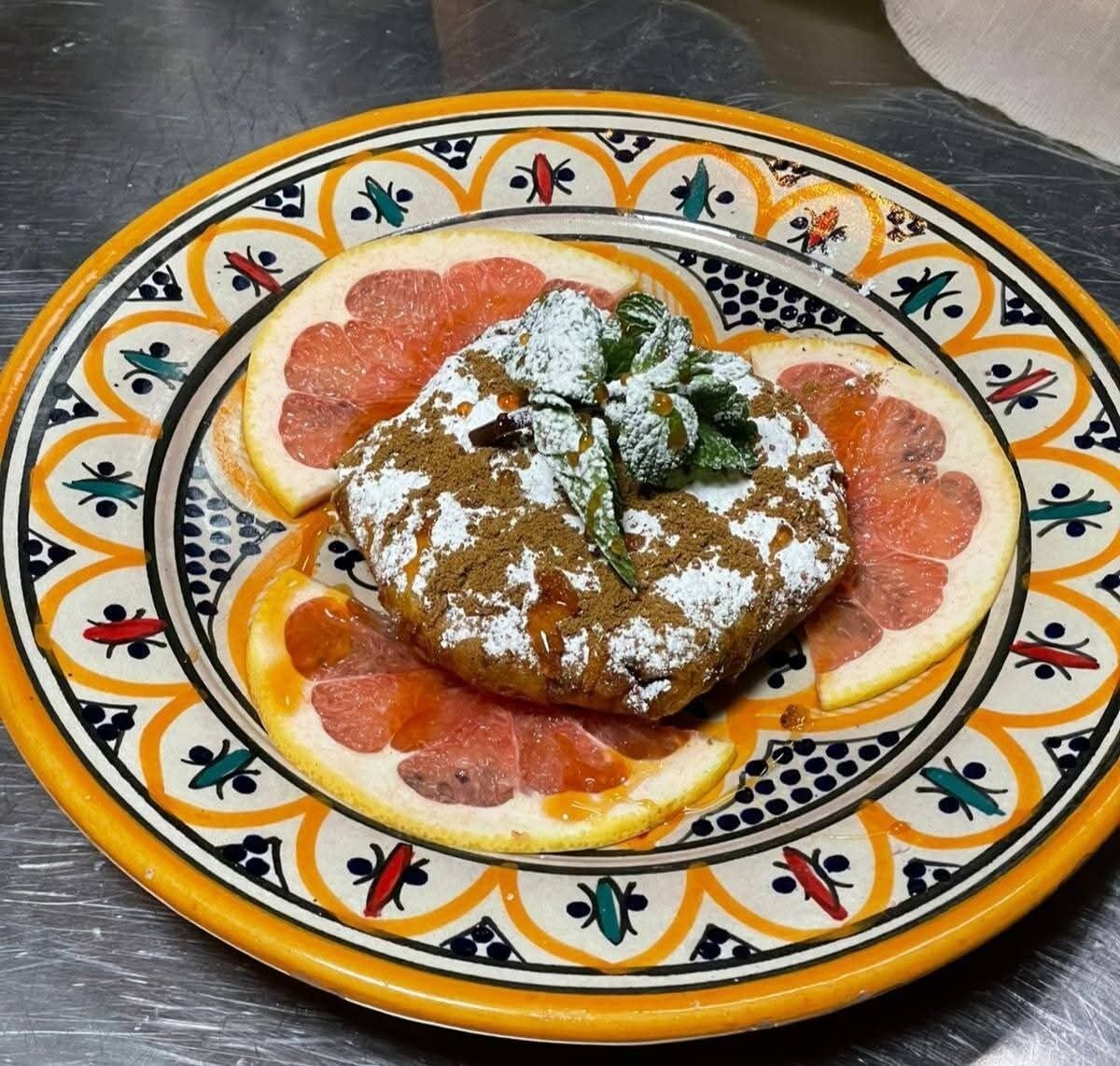 A plate with a food item, possibly a pastry, garnished with mint and powdered sugar, surrounded by slices of grapefruit on a decorative ceramic plate.