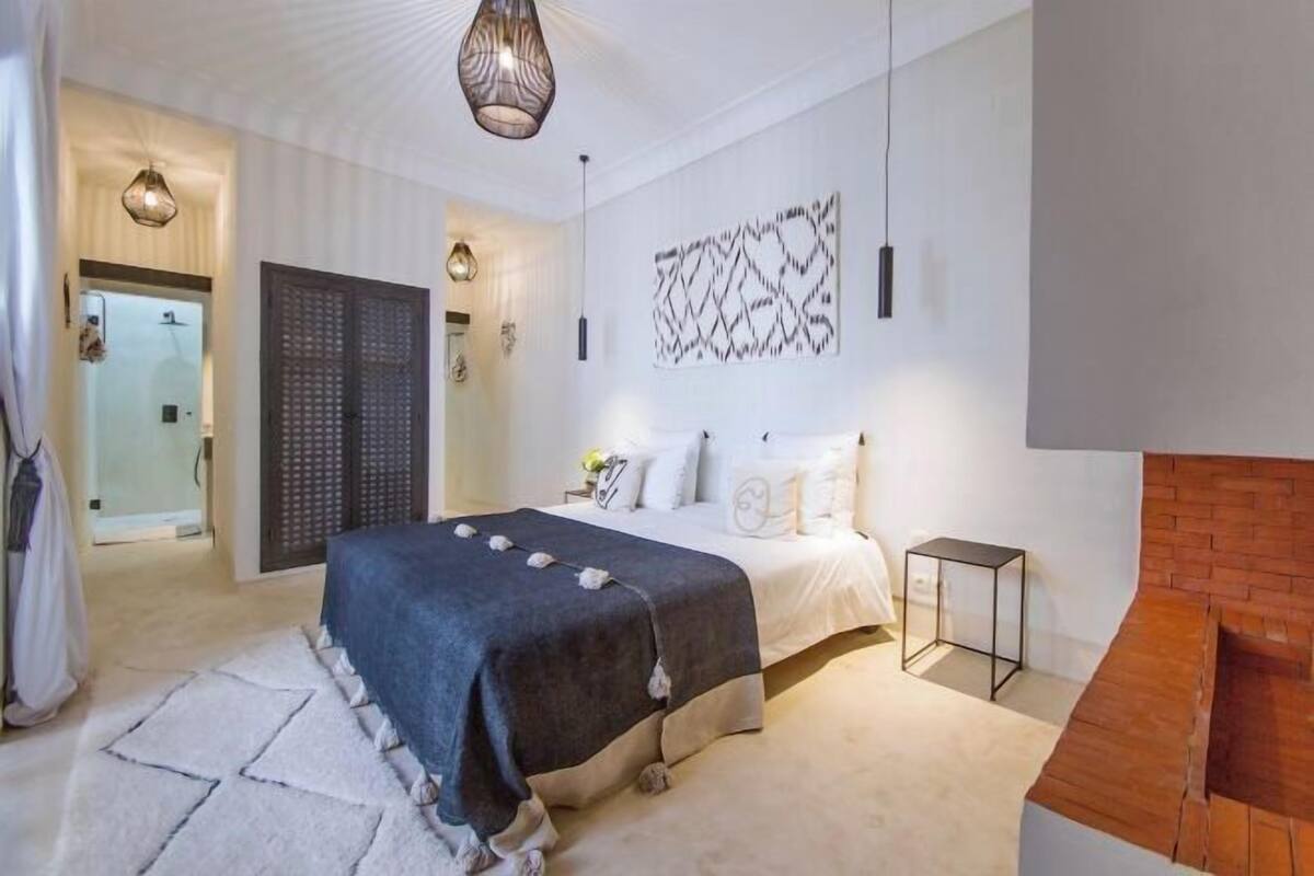 A bedroom with a bed, a bedside table, a hanging light fixture, and a wall-mounted artwork.