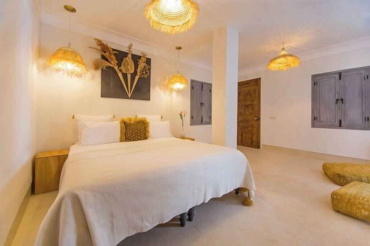 A bedroom with a large bed, two bedside tables, a wooden door, and two hanging lamps.