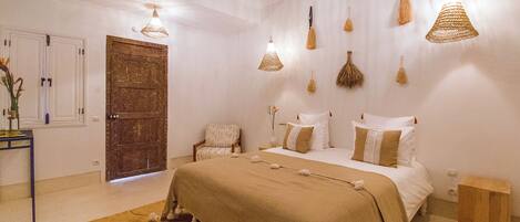 Quarto com cama, mesas de cabeceira, porta de madeira e luminárias pendentes.