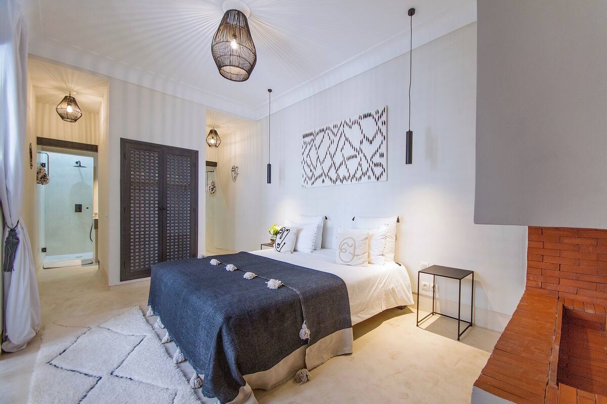 A modern bedroom with a bed, a nightstand, a wall-mounted light fixture, and a patterned wall decoration.