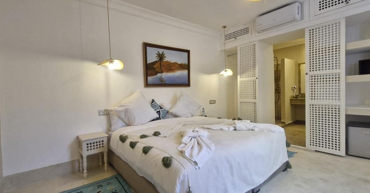 A bedroom with a bed, pillows, a nightstand, a painting, and a wardrobe.