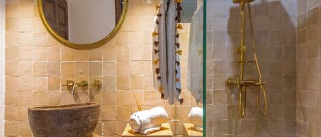 A bathroom with a stone sink, a wooden shelf, a mirror, and a shower with a glass door.