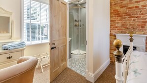 Une salle de bain avec une porte en bois, un espace de douche en verre, une baignoire blanche et un mur en briques.