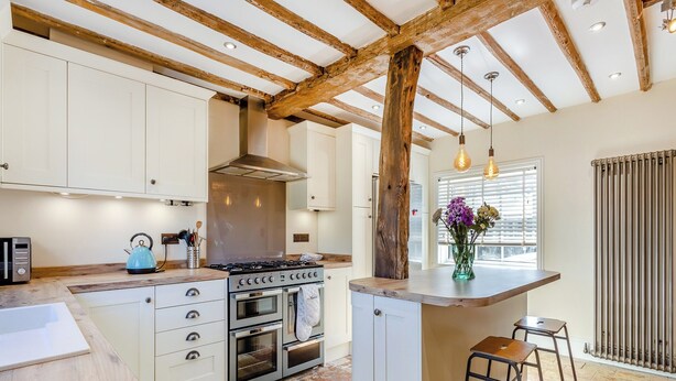 Une cuisine avec des poutres en bois, une cuisinière, un four et un petit coin bar avec des tabourets.