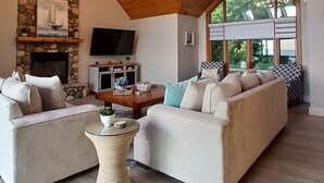 A spacious living room with a stone fireplace, a large TV, and a cozy seating area with two sofas and a coffee table. - Sunset Paradise on Lake Michigan (Charlevoix)