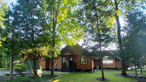 A wooden cabin with a front porch, surrounded by trees and a well-maintained lawn. - Sunset Paradise on Lake Michigan (Charlevoix)