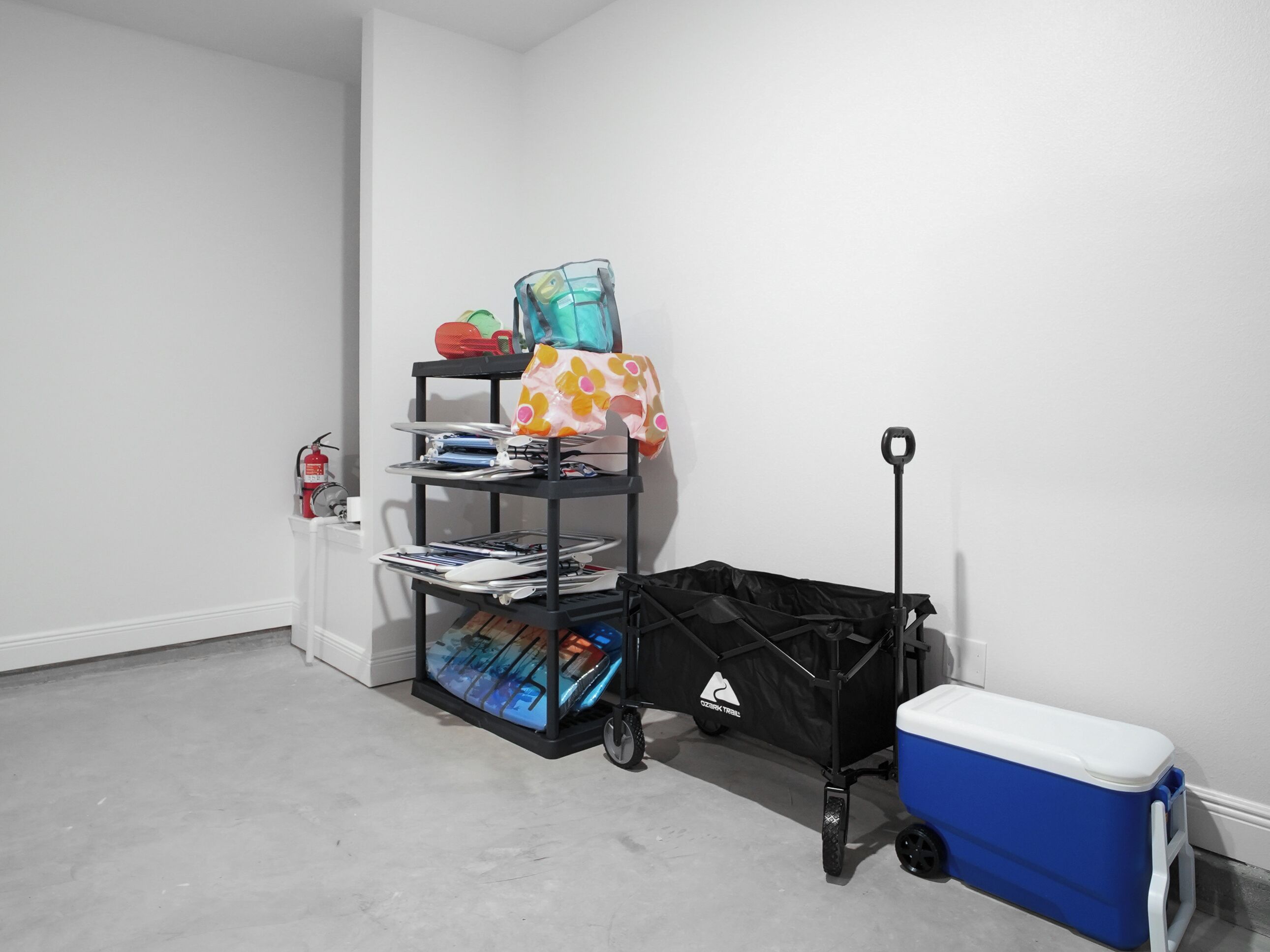 A storage area with a black cart, a blue cooler, and a fire extinguisher.