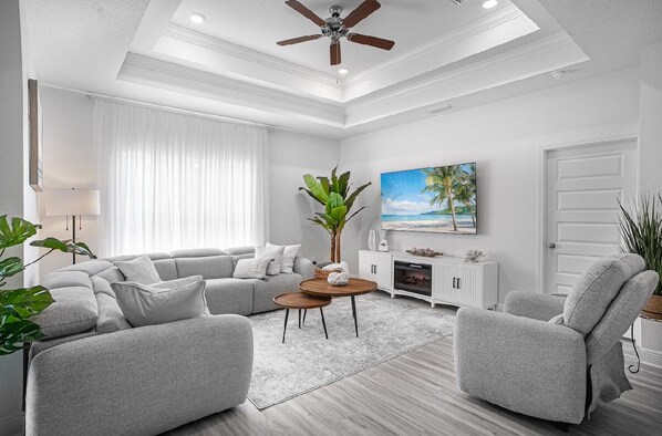 A modern living room with a sectional sofa, two armchairs, a coffee table, a ceiling fan, a painting, and a large window with sheer curtains. - Cozy 4-bedroom house near top beaches in fantastic Santa Rosa (Santa Rosa)