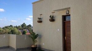 A building with a beige exterior, a wooden door, and a small garden area with artificial grass and potted plants.