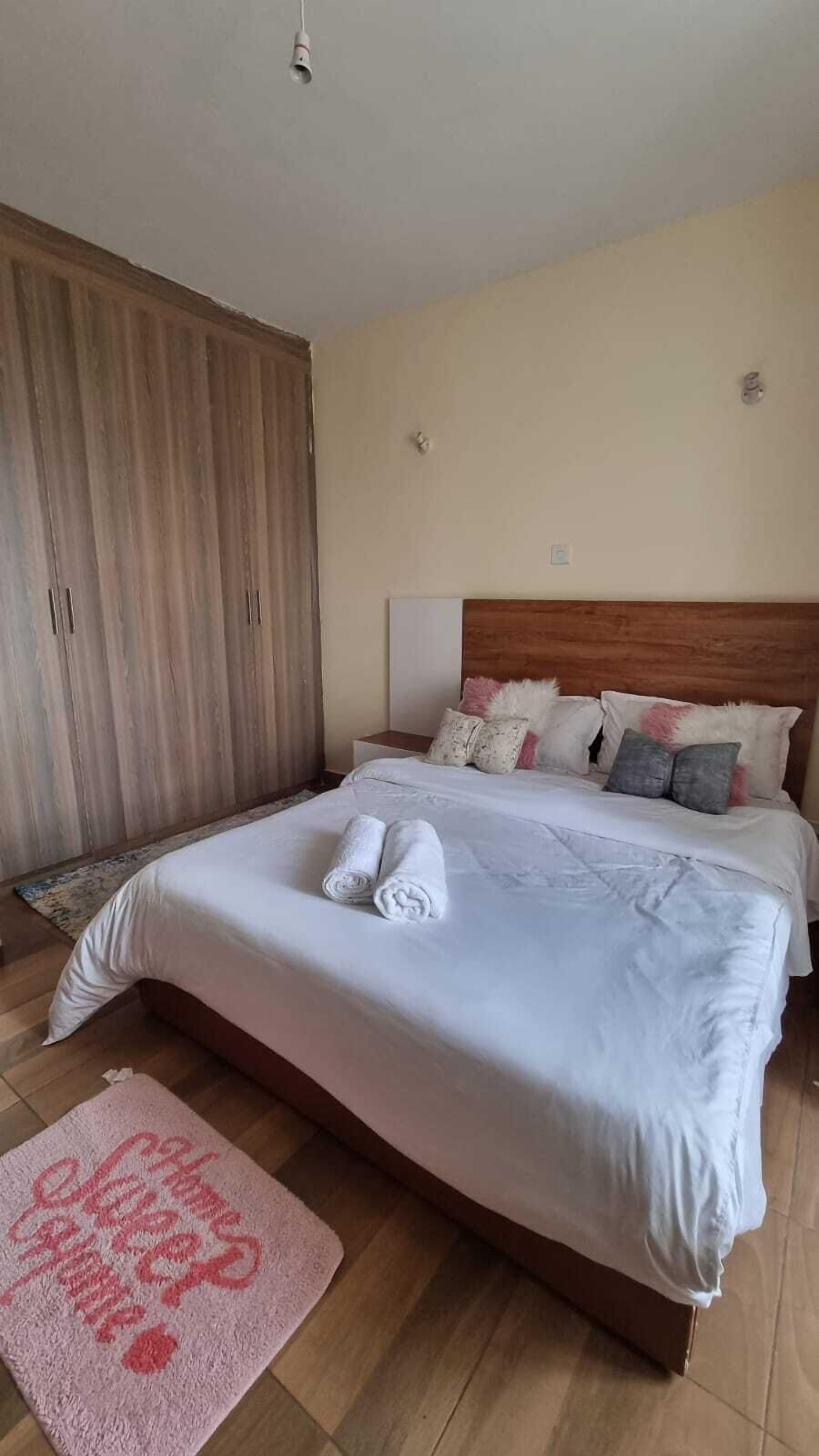 Una habitación de hotel con una cama grande, un armario de madera, una mesita de noche y una lámpara fijada a la pared.