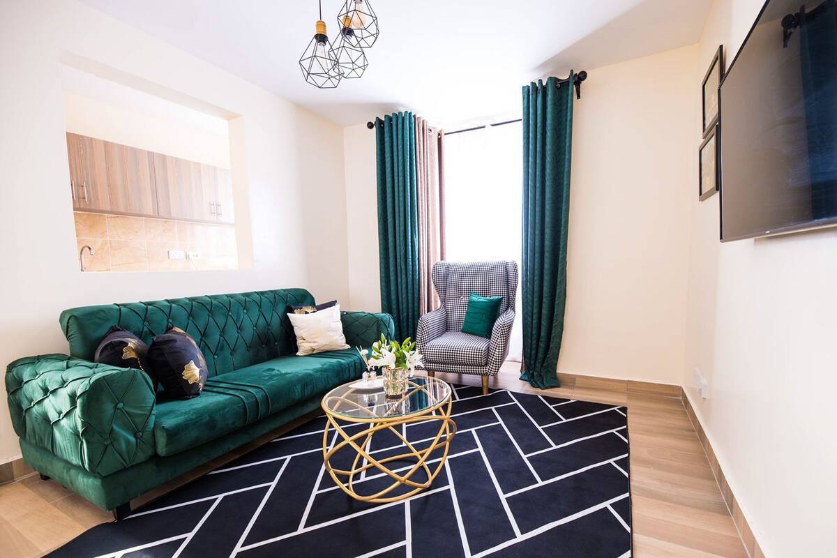 A modern living room with a green sofa, a checkered armchair, a coffee table, and a large TV on the wall.