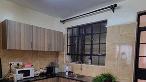 A kitchen with wooden cabinets, a black countertop, a window with blinds, and a tiled floor.