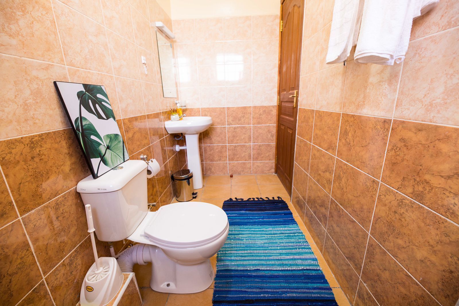 A bathroom with a toilet, sink, and a blue striped rug.