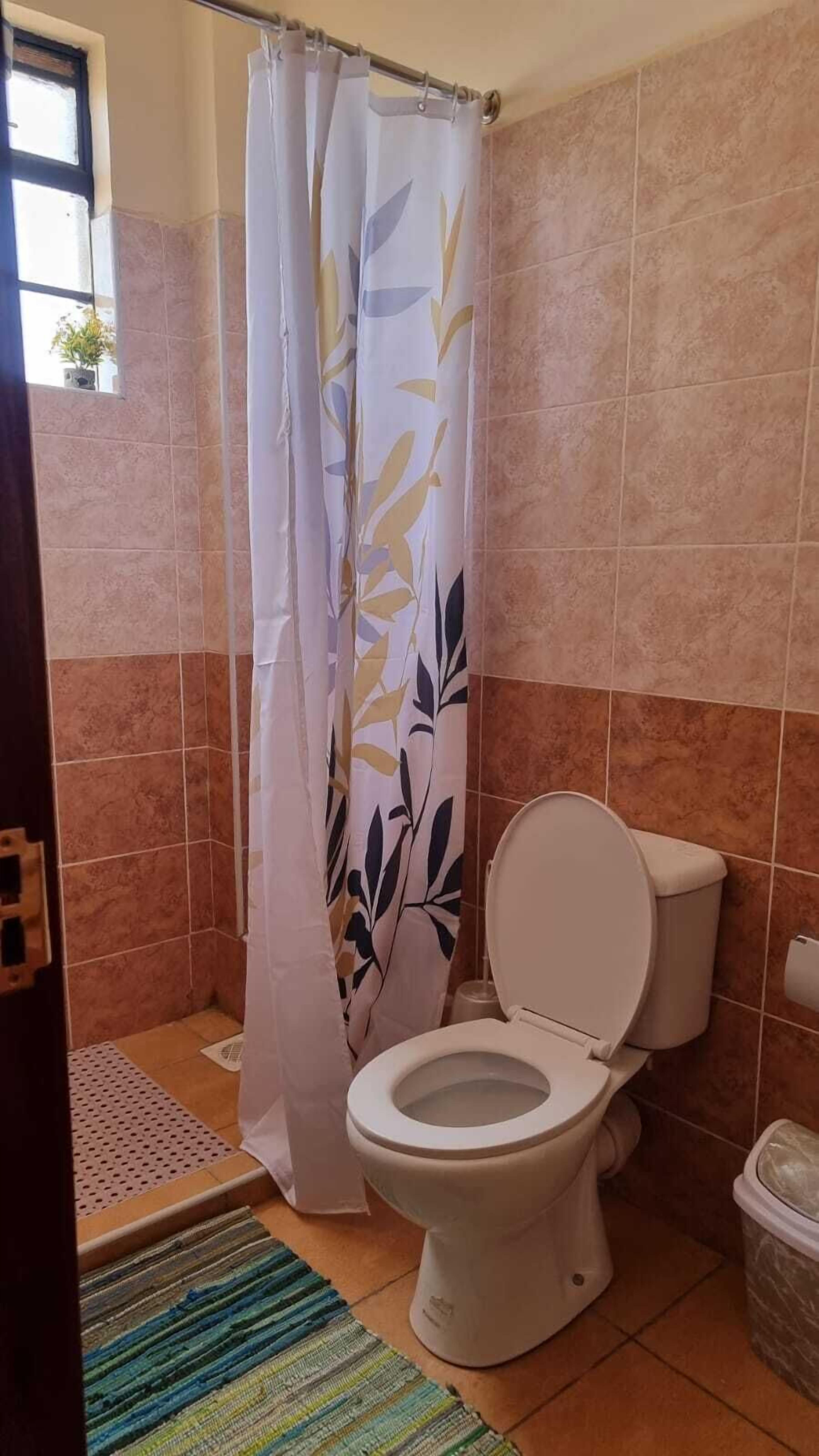 A bathroom with a toilet, a shower curtain, and a tiled floor.
