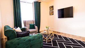 A modern living room with a green sofa, a checkered armchair, a glass coffee table, and a black and white rug.