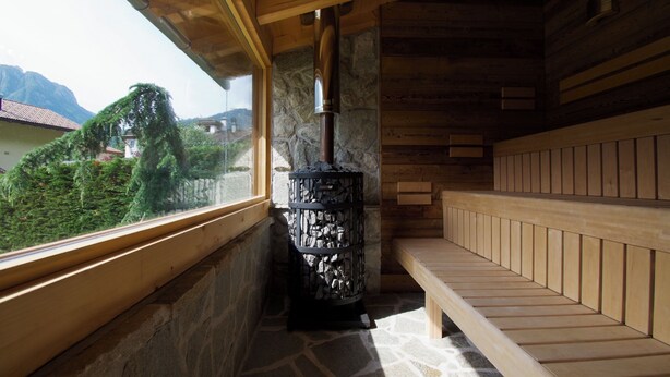 A wooden sauna with a stone wall and a bench. - Hotel Belfiore (Dimaro Folgarida)
