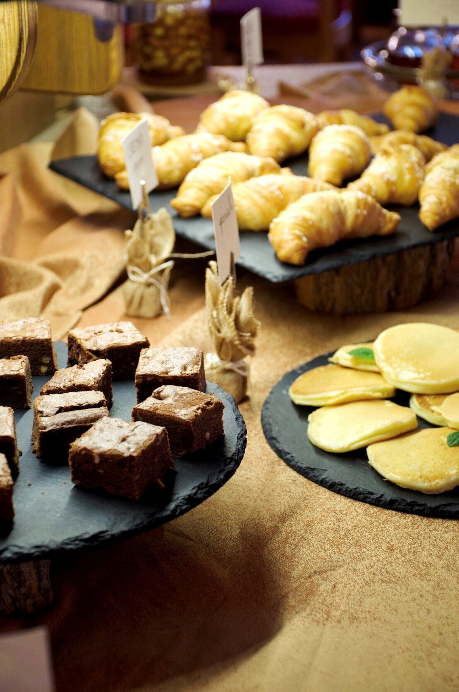 A variety of baked goods on slate serving boards, including brownies, croissants, and pancakes.