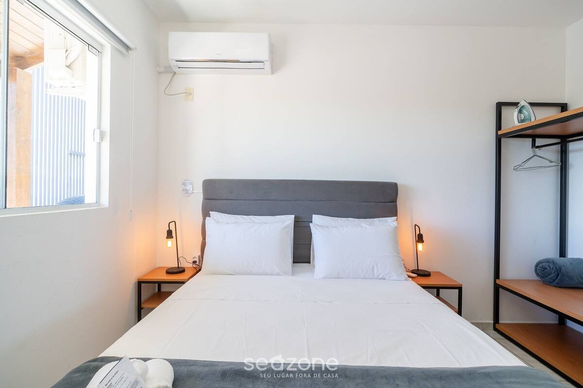 A neatly arranged hotel room with a large bed, bedside lamps, a wardrobe, and an air conditioning unit.