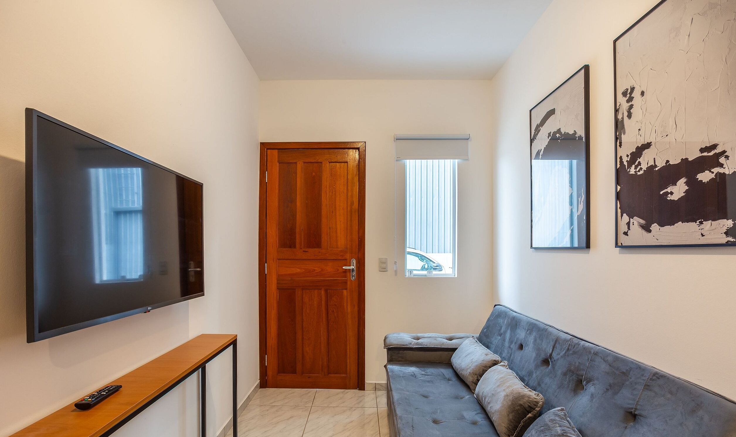 A hallway with a TV, a wooden door, a window, and a couch.