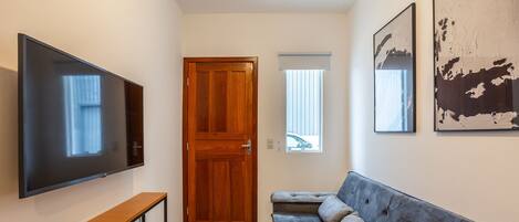 A hallway with a TV, a wooden door, a window, and a couch.