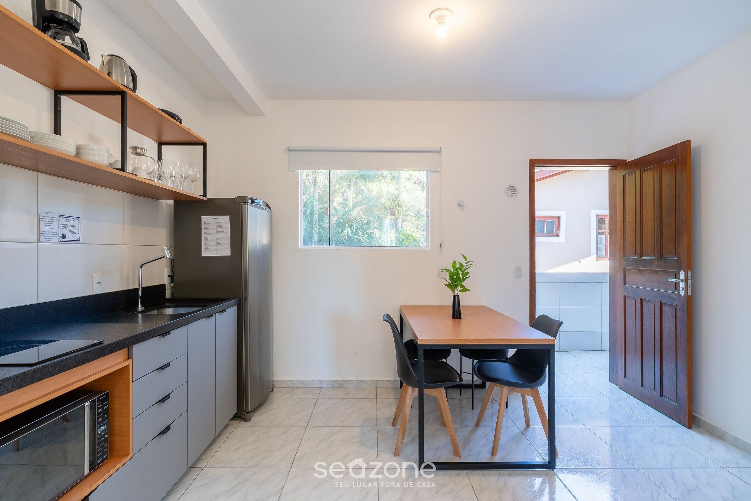 A compact kitchen with a refrigerator, a dining table with chairs, and a window with blinds.