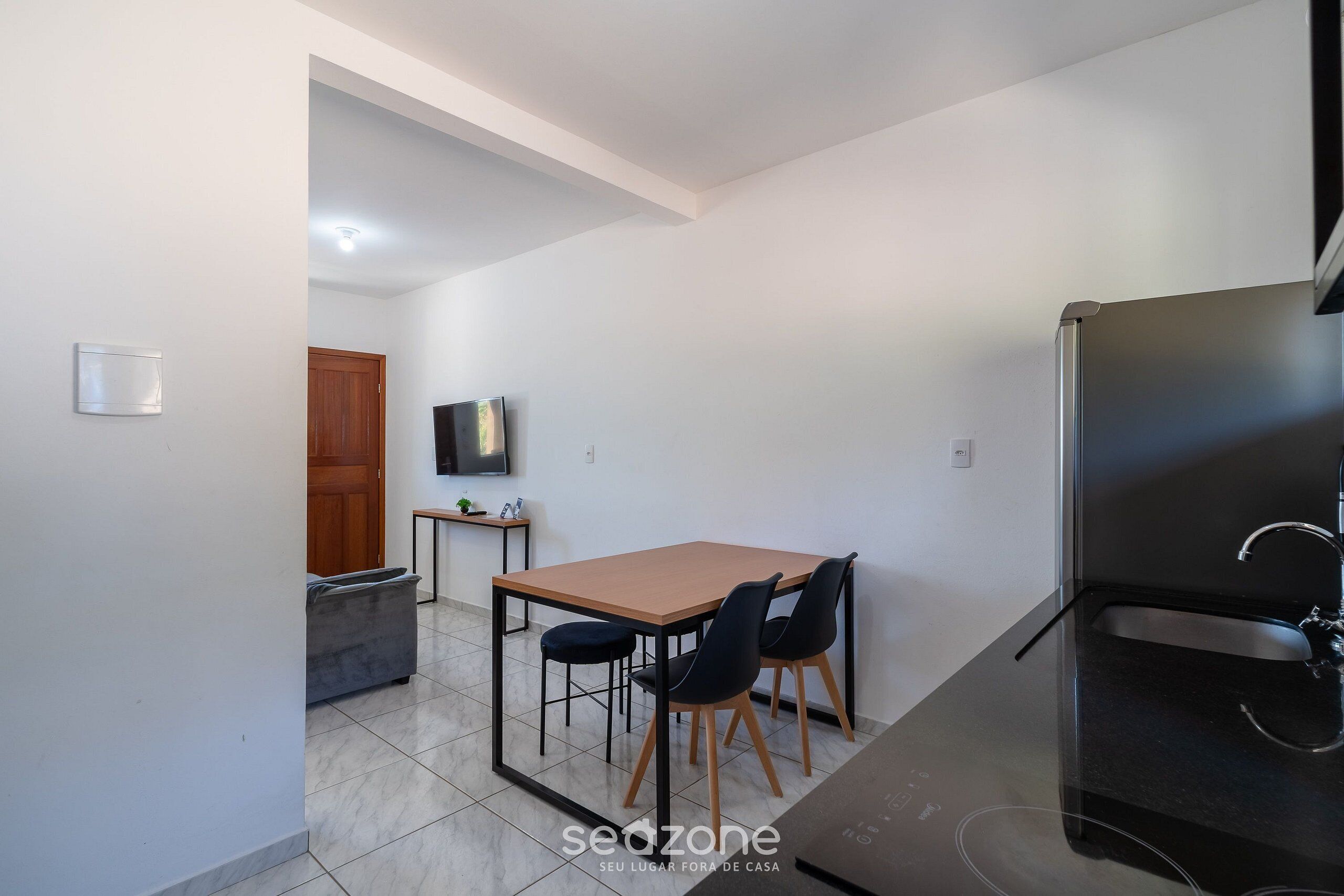 Una cucina compatta con tavolo, sedie, TV e frigorifero.