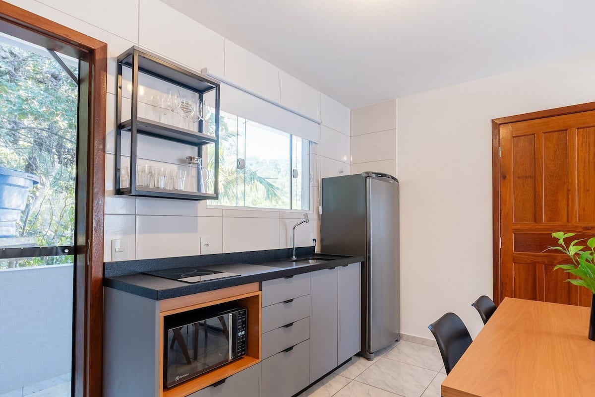 A compact kitchen with a built-in microwave, a stainless steel refrigerator, and a window with a view of greenery.