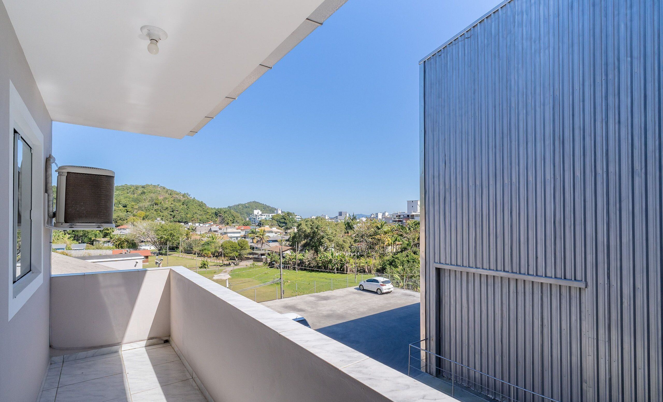 A balcony with a view of a residential area, a parked car, and a building with a corrugated metal exterior.