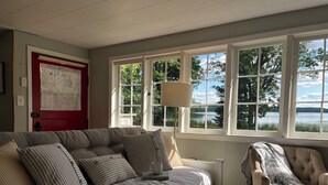 Un salon chaleureux avec un canapé, un fauteuil et une table basse. De grandes fenêtres offrent une vue sur un lac et des arbres.