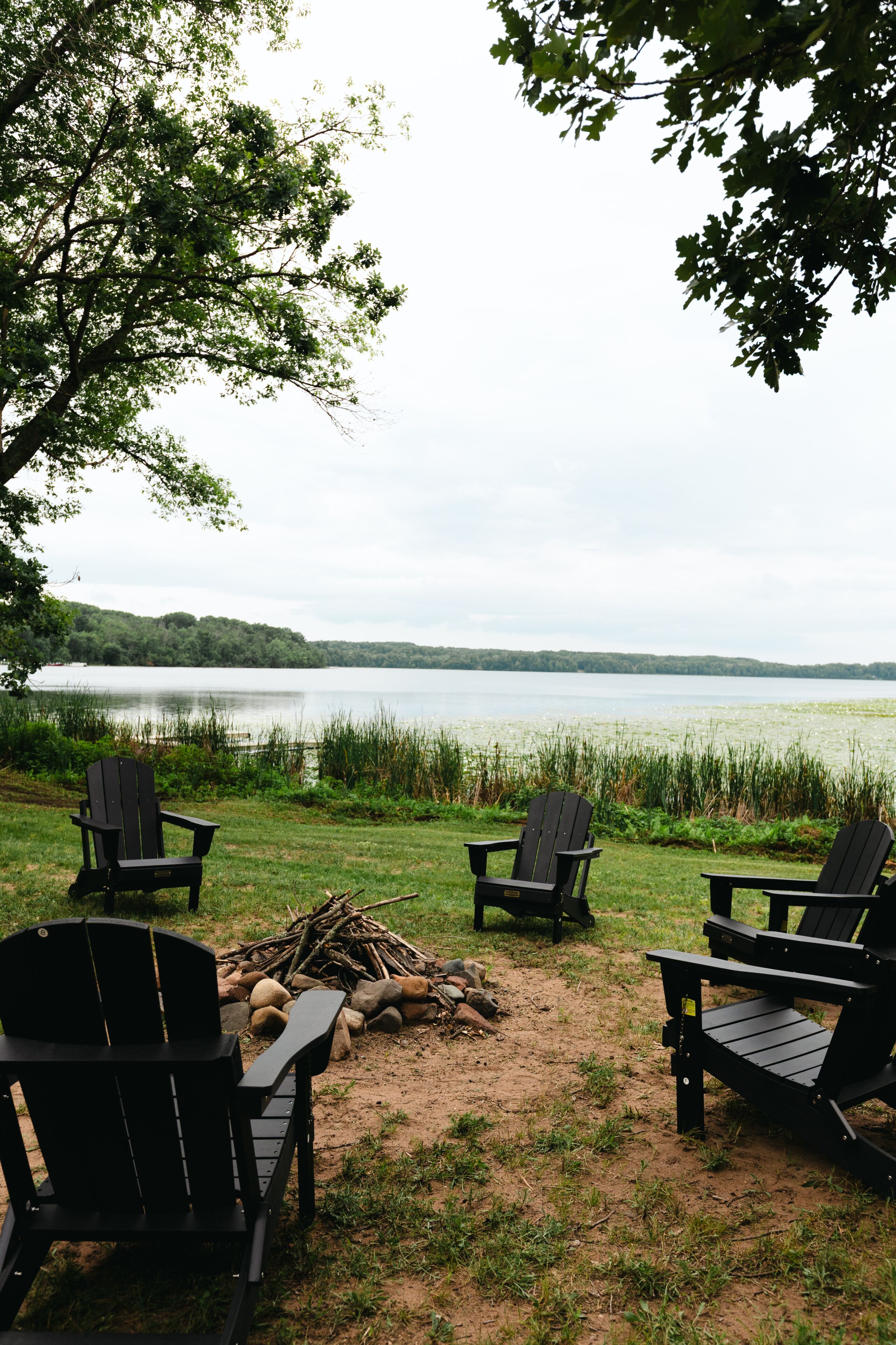 Une vue sur le lac, avec quatre chaises Adirondack, un foyer et une zone herbeuse.