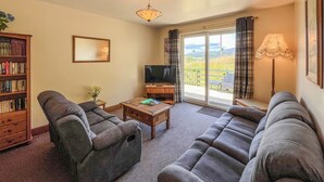 A living room with a sofa set, a television, a bookshelf, and a view through a sliding door.
