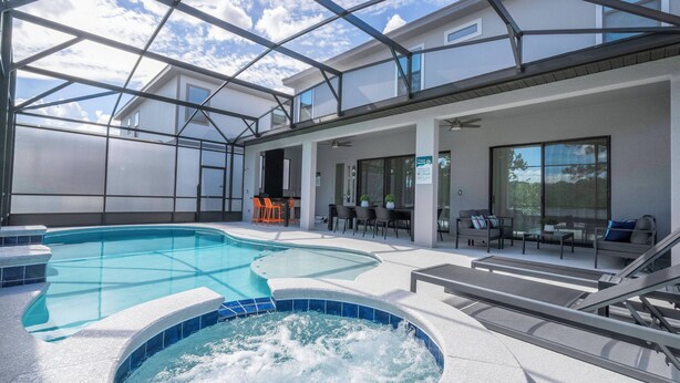 Un área de piscina interior moderna con techo de vidrio, un jacuzzi y mobiliario exterior.