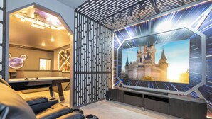 Una sala moderna con un televisor de pantalla plana grande montado en la pared, una mesa de juegos y una zona de estar acogedora.