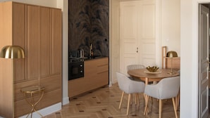A modern kitchen with wooden cabinetry, a herringbone floor, and a dining area with a round table and chairs. - Harmonia Palace - Historic Residence (Budapest)