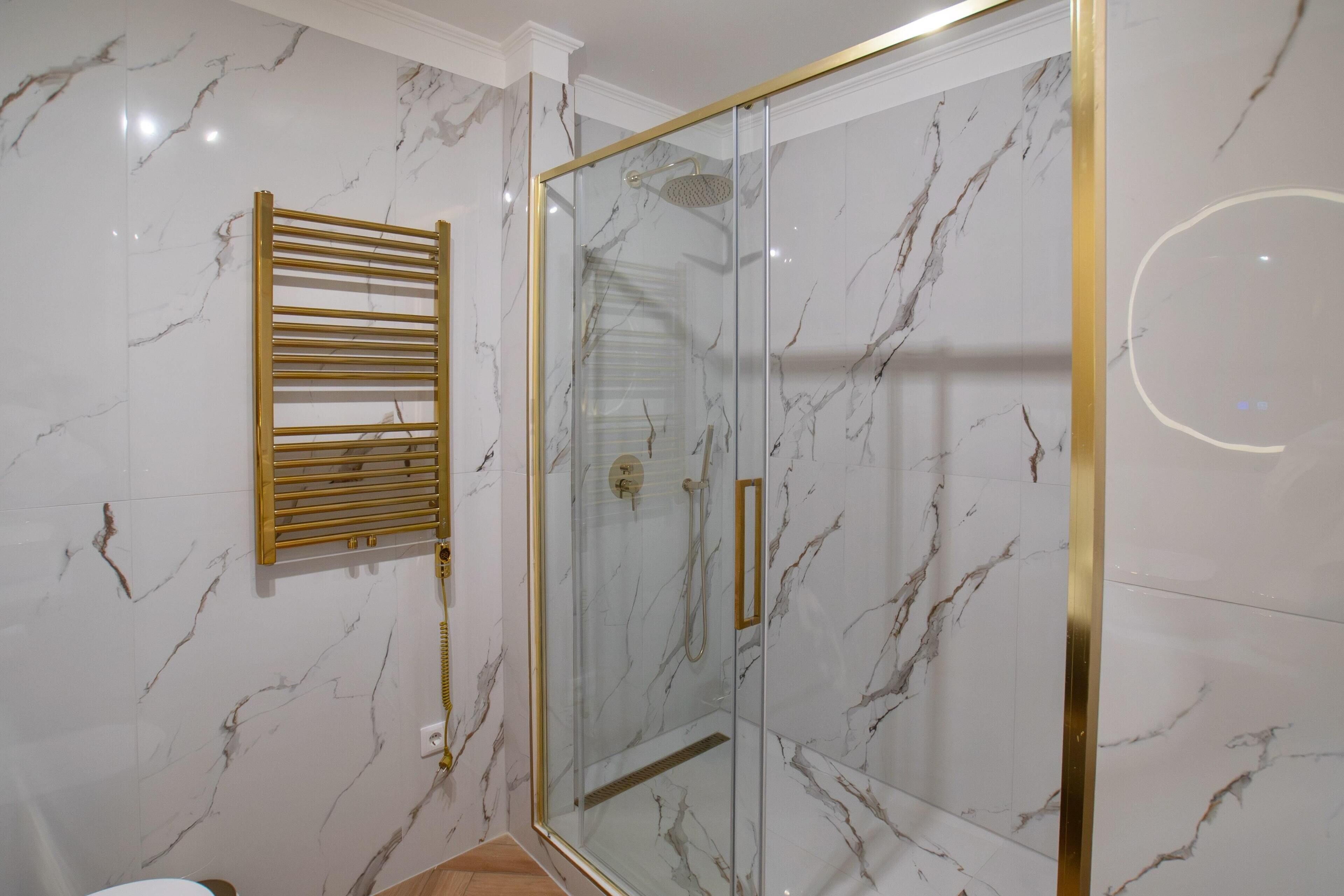Un baño moderno con ducha de vidrio, paredes de mármol y un perchero dorado.