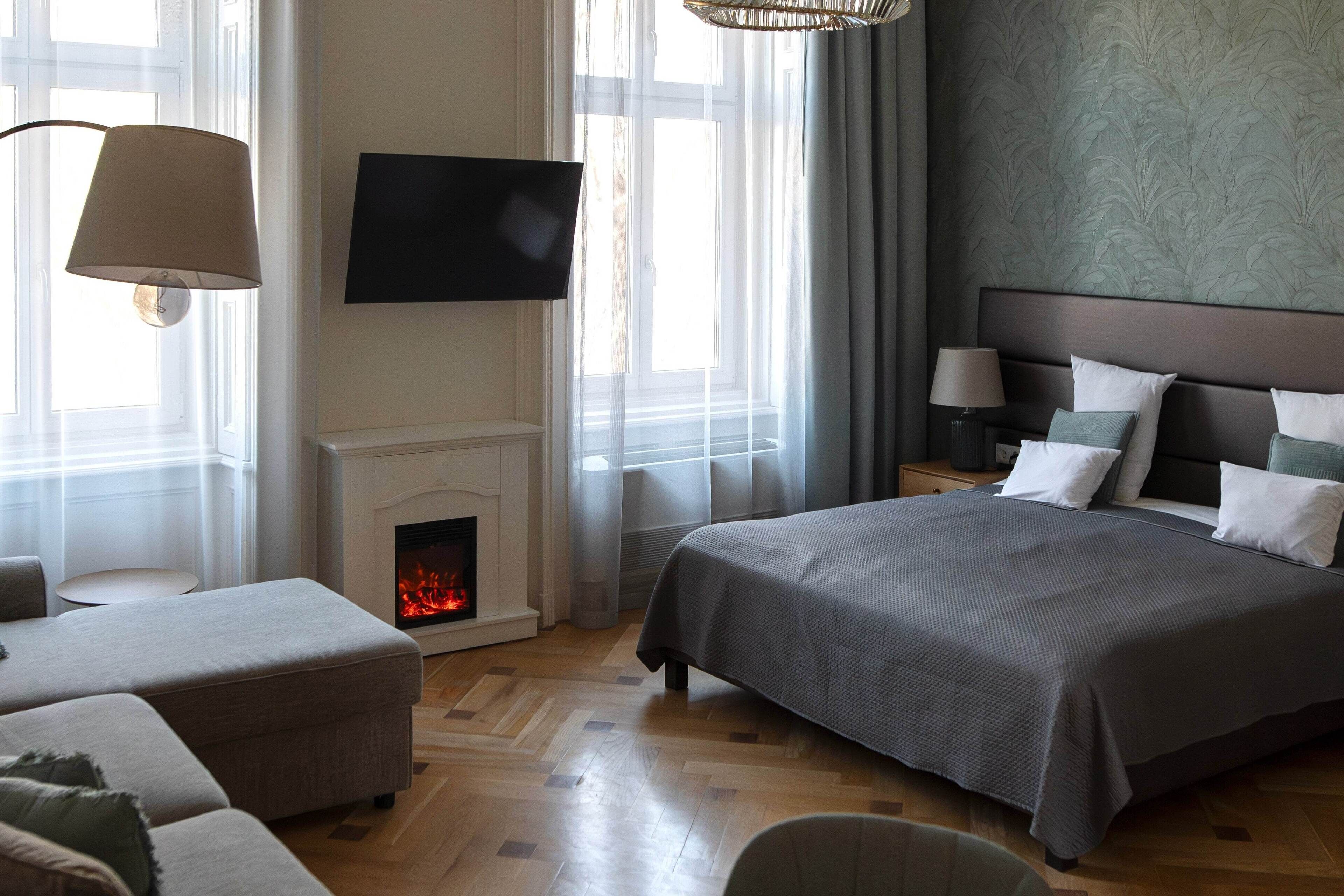 A modern hotel room with a large bed, a flat-screen TV, a fireplace, and a view of the outdoors.