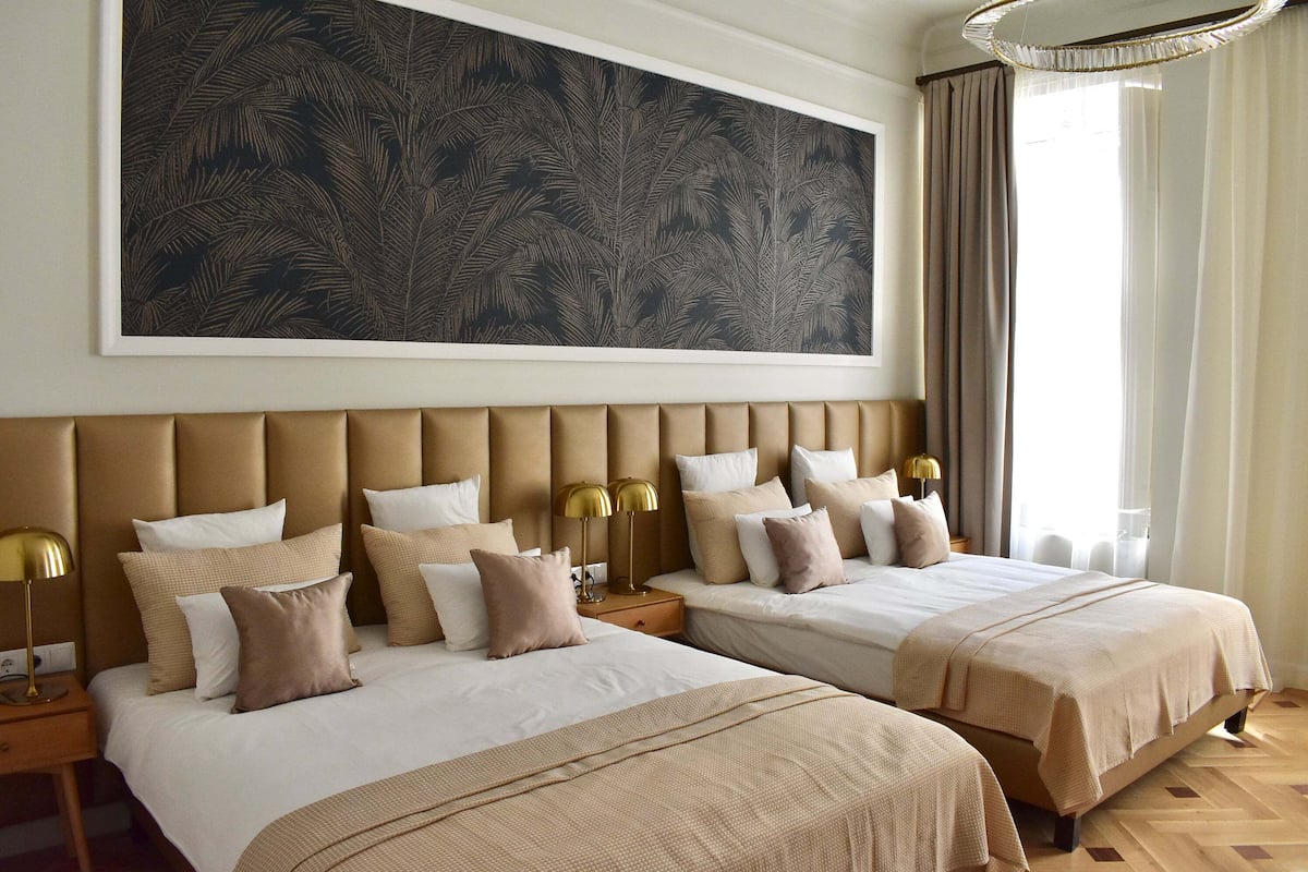 Een hotelkamer met twee bedden, een groot abstract schilderij aan de muur en een kroonluchter.