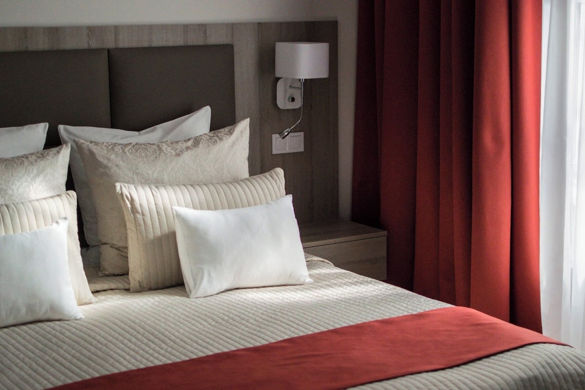 Een keurig opgemaakt bed met meerdere kussens en een rode plaid.