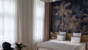 A hotel room with a large bed, a round table, two chairs, a bench, and a decorative wall tapestry. - Harmonia Palace - Historic Residence (Budapest)