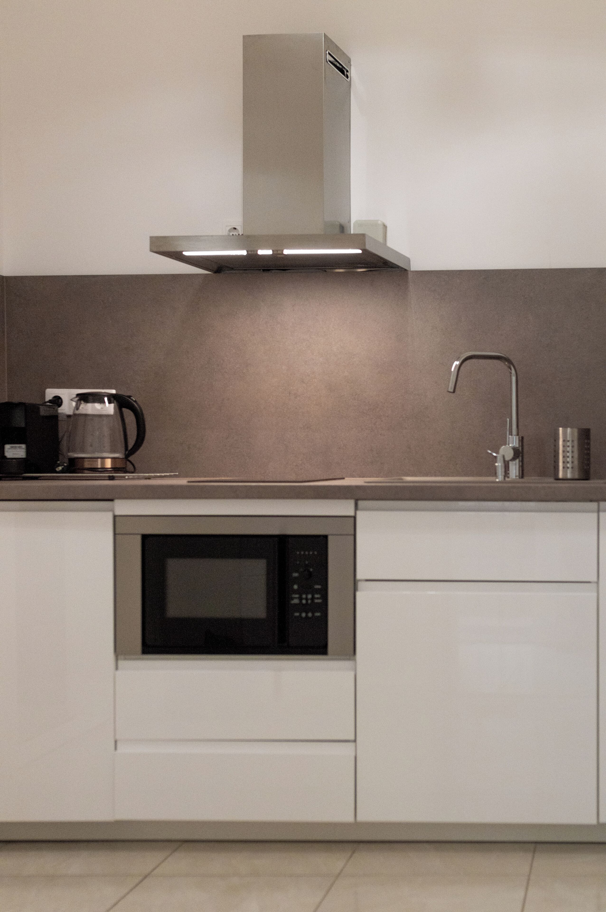 A modern kitchen with a built-in microwave, a coffee maker, and a stainless steel range hood.
