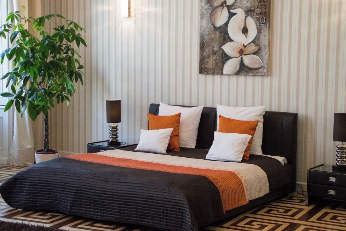 Een keurig opgemaakt slaapkamer met een groot bed, een potplant en een schilderij aan de muur.