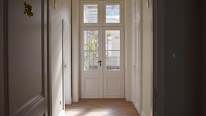 A hallway with a double door leading to an outdoor area, a wooden floor, and a small plant visible through the door. - Harmonia Palace - Historic Residence (Budapest)